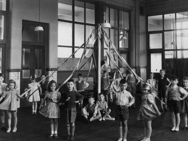 A group of children who have been practising a maypole dance, associated with May Day celebrations, and often performed by local school children. The dance involved weaving of the ribbons to form patterns around the pol. The children here are dancing in pairs, and two boys can be seen sitting sat the base of the pole to support it.