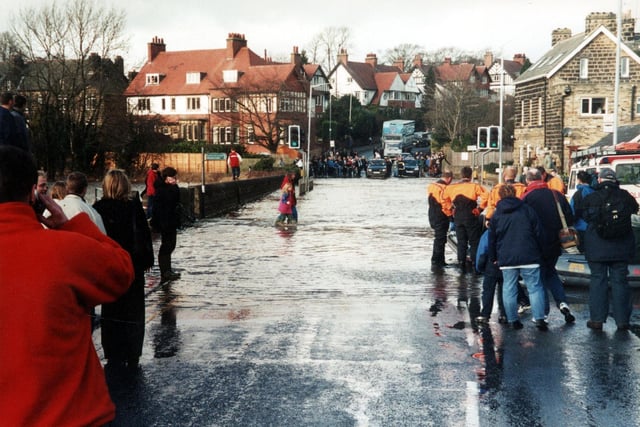 Flooding on Bridge Street at Otley in April 2002 after the River Wharfe broke its banks. People wade through the water, cars and lorries queue up unable to cross and men in orange and black wetsuits prepare a rubber dingy.
