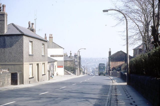 A view looking down Churwell Hill near the Commercial Inn in April 1968. Coming up Churwell Hill is a number 52 green route bus from Leeds. The Commercial Inn is known locally as 'The Top 'Oil'. The house on the left was originally a toll house which was opened in 1823. Next to that is the Fish and Chip shop which was the site of the old village smithy.