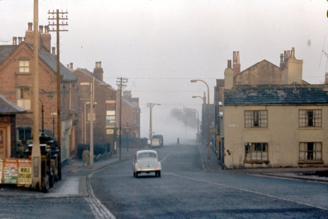 Churwell Hill in the fog in February 1962. In the foreground, left, the War Memorial is sited. Opposite the car on Elland Road there are the junctions with Old Road, left, and Little Lane, right. In front of the car on the left hand side of the road the sign for the New Inn is just visible.
