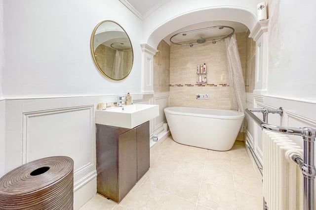 A modern bathroom includes a washbasin with vanity unit and a deep bath tub with shower over.