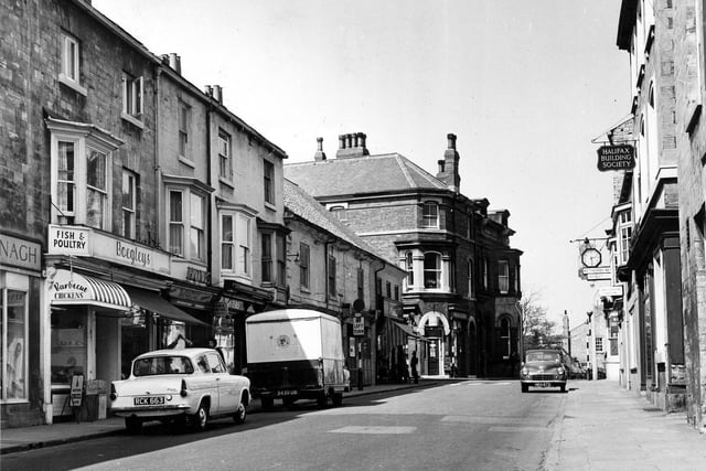 High Street in June 1962. Businesses on the left include, Kavanaghs of Wetherby, footwear retailers and Boegley's Fish, Game and Fruit. At the very right edge, part of the Brunswick Hotel, formerly the Devonshire is visible. Then there is the Halifax Building Society followed by Crossley's Printers Ltd. and the offices of the Wetherby News.