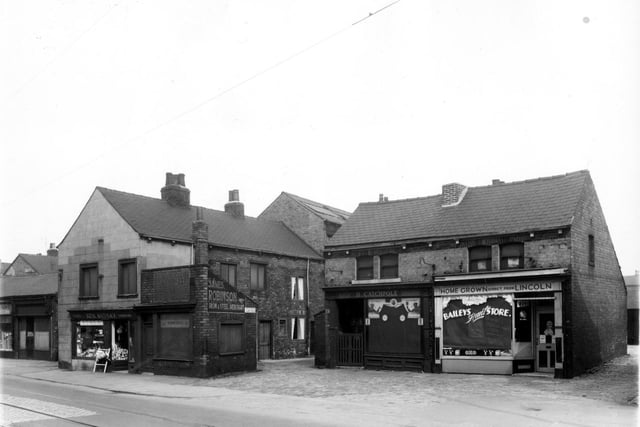 Balm Road in April 1959. On the left edge is a disused shop which had at one time been a dressmakers. Moving right there is a plumbers shop then another vacant one storey shop which had once offered boot and shoe repairs before being used by a business offering a wedding service according to a sign in the window. Continuing right is one entrance to Carr Fold.