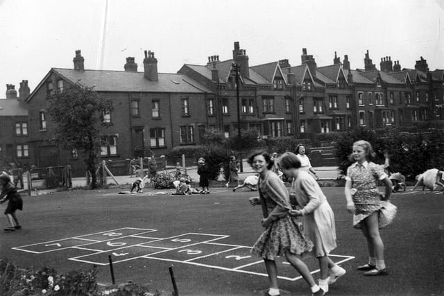 A group of three schoolgirls in the playground of Burton House, playing near an area marked out for games of Hopscotch. In the background, a terraced street of red brick back-to-back houses situated off Burton Avenue is seen. This photo dates back to 1957.