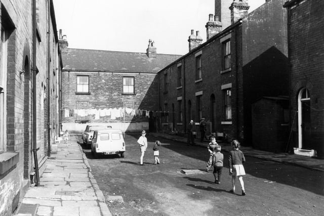 Barker Square, terraced houses located off Commercial Street, washing hangs across the street and a group of children play on the unmade road. This photo is dated April 1969.