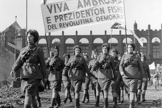 A scene being shot on location at a site off Green Lane, with Green Lane Primary School in the background. This scene, which shows a group of women marching under a banner proclaiming 'Viva Ambrosia', is part of a dream world imagined by the character Billy Fisher.