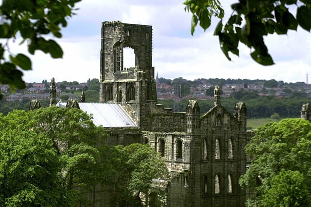 Sunlight strikes Kirkstall Abbey which stands in the suburbs  with red brick houses surrounding the ancient landmark.