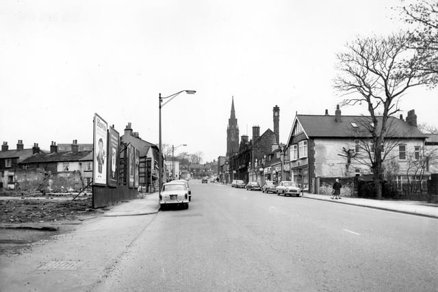Harrogate Road in April 1966. On the left a cleared area is blocked off from the road by advertising hoardings. Beyond this are houses on Ingle Row. On the right is a row of shops, library and police station and the Chapel Allerton Methodist Church.