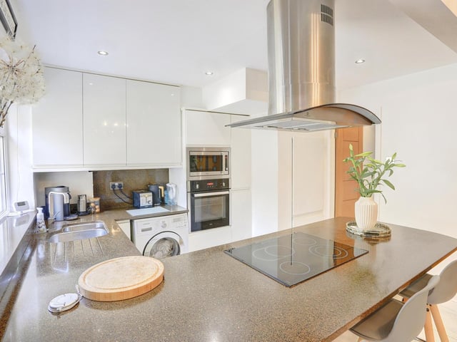 The kitchen is fitted with a range of modern white high gloss wall and base units, with complimentary work surfaces over the stainless steel sink and draining area.