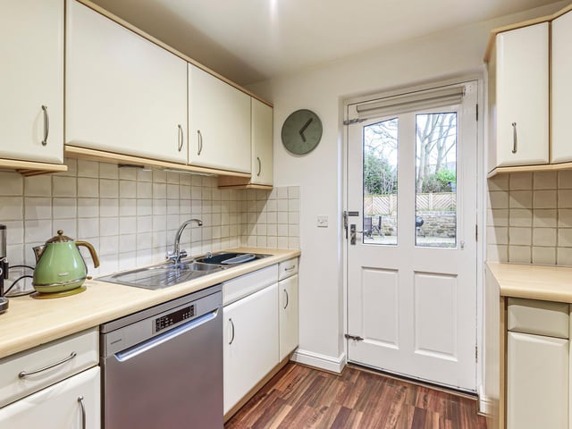 The kitchen is spacious with beautiful wooden floors and cream cabinets.