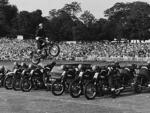 A member of the Rotal Marines Motor-cycle Display Team performs a spectacular leap over 14 men and a mini car at Leeds Gala at Roundhay Park in August 1972.