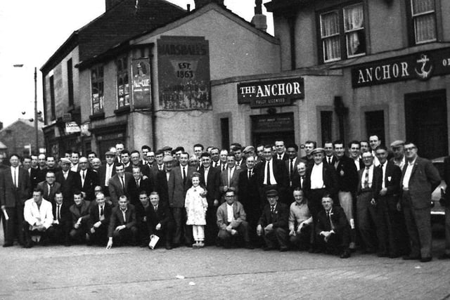 A group of men, taken outside the Anchor Inn in 1963. A young girl stands at the centre of the group on the front row.