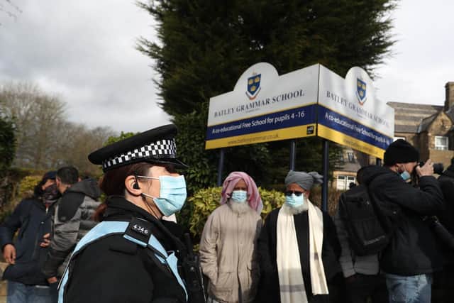 A police officer observes protesters gathered outside Batley Grammar School in Batley, West Yorkshire, where a teacher was suspended for reportedly showing a caricature of the Prophet Mohammed to pupils during a religious studies lesson in March. Photo credit:  Danny Lawson/PA Wire
