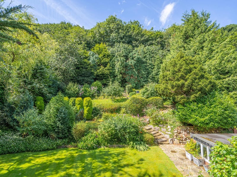 Extensive gardens with a bank of trees to the rear of the property.