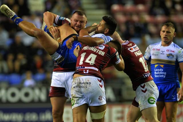 Rhinos' Rhyse Martin is upended by Wigan's Brad Singleton and Oliver Partington. Picture by Jonathan Gawthorpe.