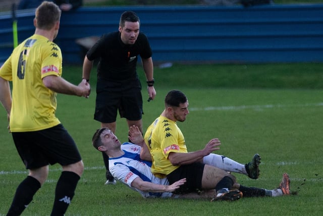 A crunching tackle is closely watched by the referee.