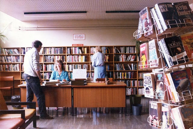 The library at St. James' Hospital providing a service for patients at the hospital. A stand of paperback books is seen on the right, with general fiction against the wall behind the counter. Pictured in June 1985.