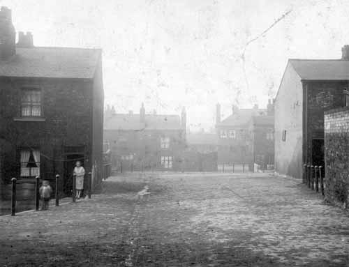 Well houses on Dolphin Street pictured in March 1930.  A mother from the doorstep of the first house to the left watches her child in the front. More terrace housing in the foreground and to the sides.