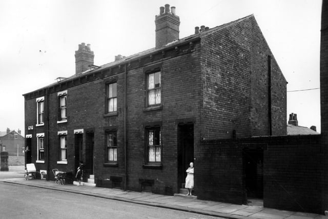 A row of four back-to-back terraced houses with cellars on Temple View Place in July 1963. On the left is Everleigh Street and on the right is a shared outside toilet block. Coach built prams stand outside numbers 96 and 98 on the left, watched over by a woman on the doorstep of number 96. Another woman stands looking out from the doorstep of number 92 on the right.