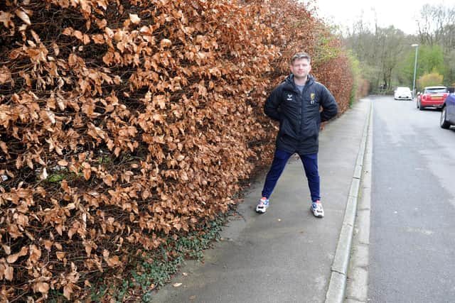 Carl Thewlis-Johns, Chairman of Moortown Rugby Club, by the overgrown bush that Leeds City Council have issued an order for him to trim.