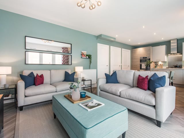 The open kitchen-diner features contemporary cabinets in a contrast finishes, and glass six-seater dining table, while the family area of this open-plan space features two stone sofas with splashes of teal, berry and navy in the accent wall colour and soft furnishings. The lounge includes a stunning corner sofa, textured feature wall and navy accent chair.