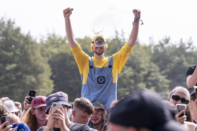 A festivalgoer in a Minion outfit gets up on a friend's shoulders for a better look.