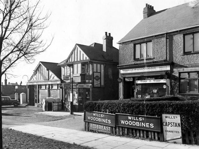 Shops on Harrogate Road - 401 J.A. Walker automobile engineer, 403 R.S. Rudd newsagents and sub post office and 405 J. Eamonson household stores. Advertisements for Wills Capstan cigarettes, woodbines, Cadbury's, Turf cigarettes, Craven A and Gold Flake. A car and bicycle are near a petrol pump on the left. Pictured in February 1952.