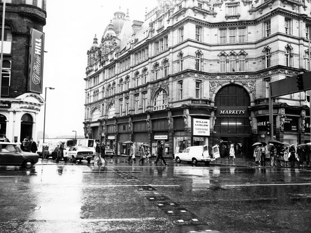 Looking east from Vicar Lane towards Ludgate Hill, with Kirkgate Market on the right. On the Ludgate Hill side of the market entrance is Willis Ludlow, department store, and on the Vicar Lane side is Barker's children's wear and baby linen. The National Westminster Bank can be seen on the right of the photograph. The photo was taken on a wet day in January 1979 and there are many people with umbrellas.