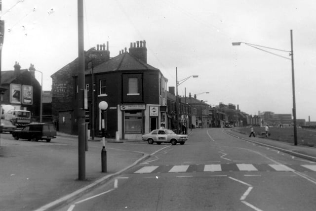 Looking east along Burley Road with the junction with Hyde Park Road to the left. On the corner is Smith's Cafe at no.134 Burley Road. Behind this can be seen the side of Andrew Commercial Hotel at no.130. A police car is turning the corner and there is a zebra crossing in the foreground. Pictured in August 1975.