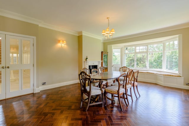 The dining room with parquet floor is filled with natural light from a wide bay window.