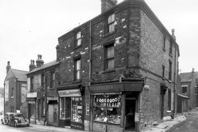 Delph Lane in September 1959. On the left is the junction with Woodhouse Street. The building at the corner is number 202, the White Rose public house. Painted signs on the back and side of the pub are for Melbourne beers. Moving right on Delph Lane, number 1 is occupied by 'Jeannie', a hairdressers. Next, 1a is the property with the double gates which lead to a yard area. Lee Ward Television Co. are based at number 3, there is a washing machine in the window. This type was basically an electrically heated tub with a post in the centre which agitated the clothes in the water. A wringing machine was positioned over the tub. At the corner with Woodhouse Cliff is 5 Delph Lane. This is James Fielders greengrocers selling 'Choice fruits, flowers, vegetables, fresh fruit, poultry and rabbits'. On the right is part of Woodhouse Cliff.