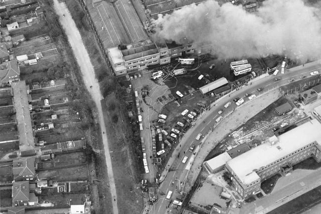 A bird's eye view of Cross Gates Carriage Works on Manston Lane, the firm of Charles H. Roe. A small fire is being attended to by several engines in March 1975. Nine metro buses worth £120,000 each had to be pushed to safety. Charles H Roe's company was formed in 1916. After closure in the 1980's new investment was generated and buses are still being built here under the name of Optare Lted. Curving down from the right edge is Manston Lane. Barnbow Royal Ordnance factory is bottom right.