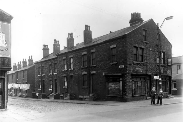 Binks Street, a row of back-to-back terraced houses in August 1958. Clothes hang on a line stretched across the street whose junction is with Armley Road. At the corner two boys stand at an L.C.T. Bus Stop.