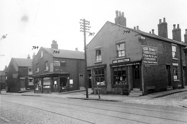 Balm Road, cobbled with tram lines, in September 1935. Number 39, the Railway Hotel, can just be seen on the extreme left. Then is Wright Street, with one house showing. Number 45 is Bertie Colin Crookson, draper; number 47 is Joseph Richardson, greengrocer (on the corner of Wainwright Street). Above the shop are metal signs for Brasso Polish and Zebra Grate Polish. Number 49 is Edward Batty, fishmonger, who has a tiled window display. A man stands in the doorway. Number 51 is Squire Bramley, undertaker, who has a sign showing his telephone number and a large one on Wainwright Row saying he has had '23 years with the late J. Charlesworth'.