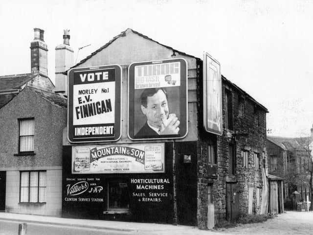 A view of number 6a Church Street, a three storey terraced property in April 1967. On the gable end are a number of advertising signs including, Turog big taste brown bread, W. Mountain and Son Ltd, Agricultural Horticultural Engineers, and an election poster, Vote Morley number 1 E.V. Finnigan, Independent'.