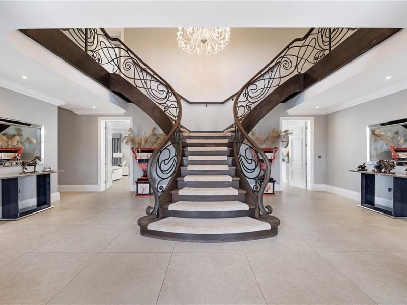 A striking portico leads into the reception hall, where a Hollywood-style split staircase with ornate balustrade forms a dramatic centrepiece.