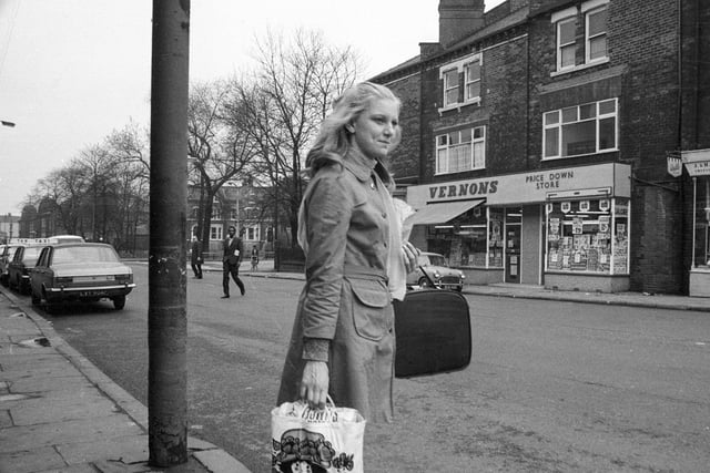 Roundhay Road looking towards the junction with Spencer Place in 1969. A young woman carrying a shopping bag is waiting to cross the road. Shops opposite are numbered 81-83 Roundhay Road and include Vernons 'Price Down Store' and a sweet shop beginning with 'J. & H.' but we were unable to find a confectioners' listed with these initials. In the background on Spencer Place are three storey terraced properties with steps up to the entrances and large bay windows. Beyond these the domed building is the former Leeds Institute for the Blind school at 79 Roundhay Road whilst the building on the extreme left is possibly the Prince Arthur pub.