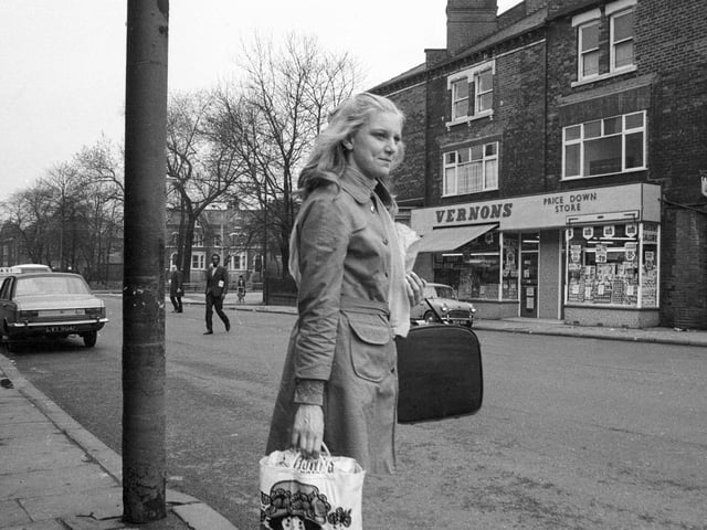 Roundhay Road looking towards the junction with Spencer Place in 1969. A young woman carrying a shopping bag is waiting to cross the road. Shops opposite are numbered 81-83 Roundhay Road and include Vernons 'Price Down Store' and a sweet shop beginning with 'J. & H.' Beyond these the domed building is the former Leeds Institute for the Blind school at 79 Roundhay Road whilst the building on the extreme left is possibly the Prince Arthur pub.