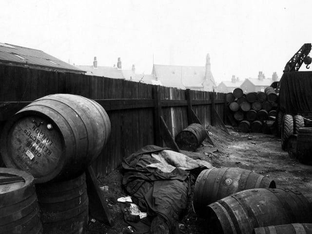 The yard of Archbolds Haulage on the corner of Leathley Road and Cross Myrtle Street showing large barrels stacked in the corner and a large crane in the background. The yard has a high wooden fence. Roofs of houses beyond can be seen over the top of the fence. Pictured in April 1947.