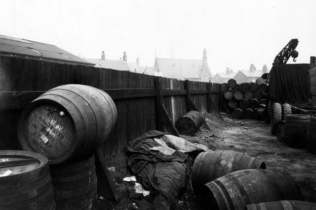The yard of Archbolds Haulage on the corner of Leathley Road and Cross Myrtle Street showing large barrels stacked in the corner and a large crane in the background. The yard has a high wooden fence. Roofs of houses beyond can be seen over the top of the fence. Pictured in April 1947.