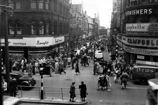 A view looking south along Lands Lane from The Headrow in July 1956. Benefit footwear, Mallories wine and spirit merchants, Campbells home furnishers, Theatre Royal, Ross furs, John Peter's, Albion Place and church visible.
