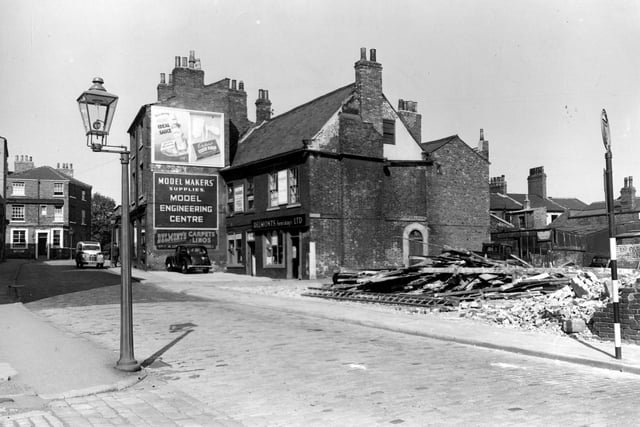 Wade Lane in September 1953. View looking north east at east-south-east side and number 42. Delmonts Furnishings Limited occupies two brick buildings. In background there is a 3 storey Georgian style house, two parked cars and in foreground are remains of demolished building, a road sign and street light.