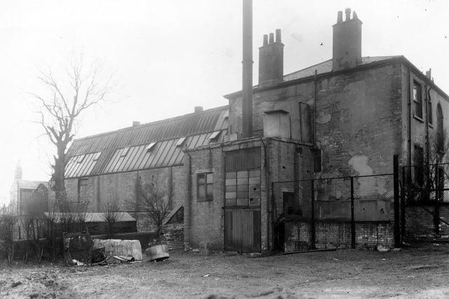 The Sunshine Laundry located on Wilson Place, from adjacent land. It was established in 1931 in the former home of the Wilson family, Armenian Lodge, the larger building on the right. The garden of the house was the site used for the additional building, with its partially glazed roof, left. Various items of scrap are piled up in front of a low stone wall. Pictured in March 1960.