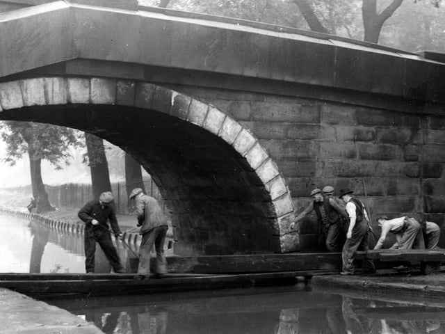 This view shows Redcote Bridge over the Leeds and Liverpool Canal. Workmen are demonstrating the 'canal boom'. Redcote Lane runs across the bridge. A man is fishing in the background by some trees. Pictured in August 1942.