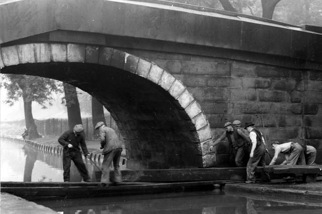 This view shows Redcote Bridge over the Leeds and Liverpool Canal. Workmen are demonstrating the 'canal boom'. Redcote Lane runs across the bridge. A man is fishing in the background by some trees. Pictured in August 1942.