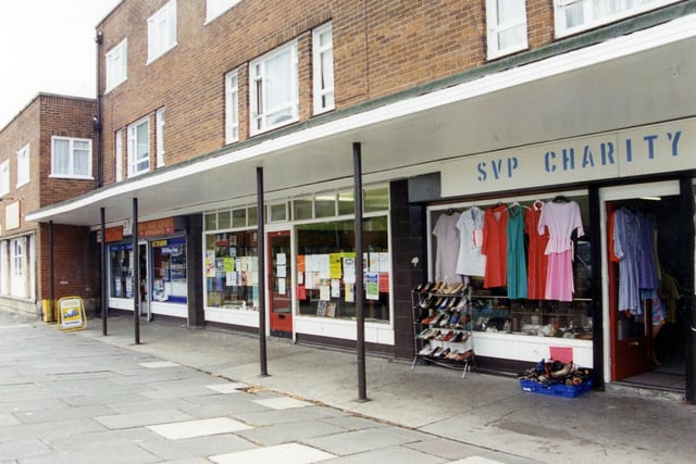 SVP Charity Shop in Armley with clothes and shoes displayed outside. Next to this is Armley Heights Library, one of Leeds City Libraries' small branches, then Dewhirsts newsagents and post office.