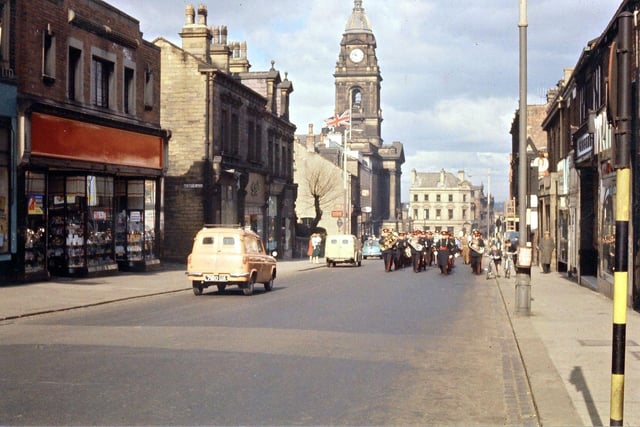 The procession can be seen marching along Queen Street with the Town Hall visible in the background. Note that the Town Hall flag is flying at half mast; that the entry into the Zion Chapel church yard with its pollarded tree is still in existence; that the entrance to Beryl Burton Gardens is still called Henry Place and that the letters for F. W. Woolworth had been taken off their red background in order to be regilded. This was done every year. The Salvation Army Citadel Band, from Ackroyd Street in Morley, is leading the procession.