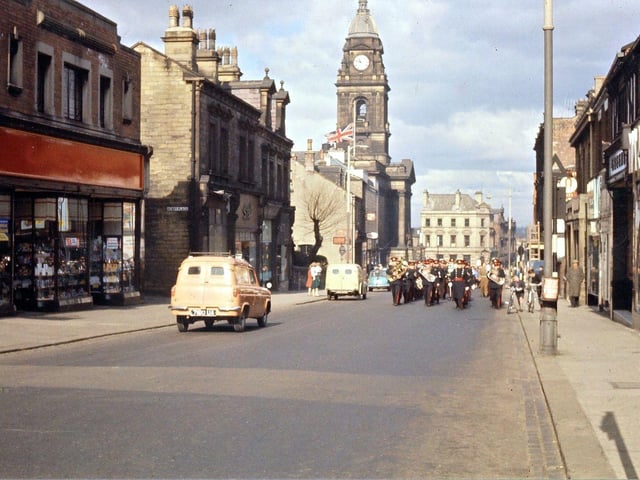 The procession can be seen marching along Queen Street with the Town Hall visible in the background. Note that the Town Hall flag is flying at half mast; that the entry into the Zion Chapel church yard with its pollarded tree is still in existence; that the entrance to Beryl Burton Gardens is still called Henry Place and that the letters for F. W. Woolworth had been taken off their red background in order to be regilded. This was done every year. The Salvation Army Citadel Band, from Ackroyd Street in Morley, is leading the procession.