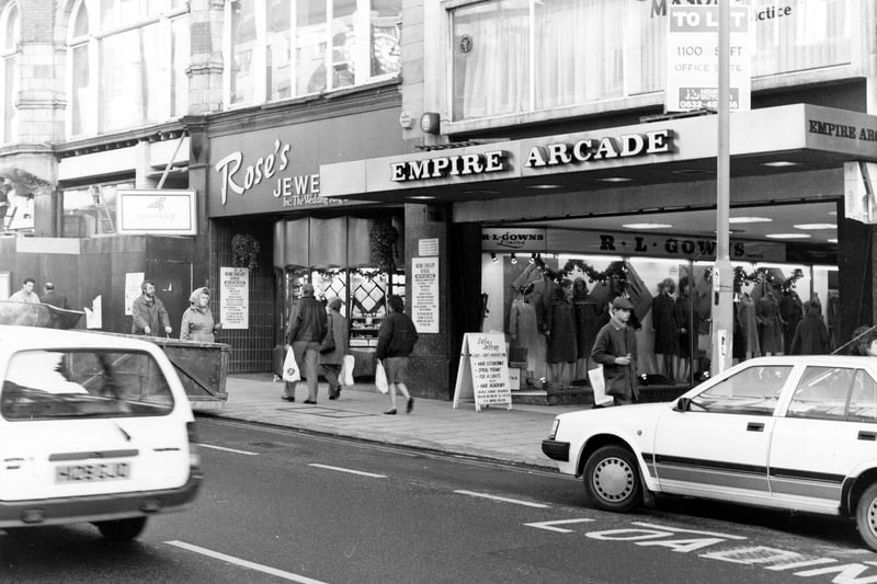 The east side of Briggate showing the entrance to the Empire Arcade. This was opened in 1964 on the site of the old Empire Theatre; in 1996 it was redeveloped to become Harvey Nichols. R.L.Gowns, ladieswear, can be seen in the arcade. Next to it on Briggate is Rose's Jewellers.