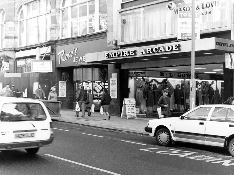The east side of Briggate showing the entrance to the Empire Arcade. This was opened in 1964 on the site of the old Empire Theatre; in 1996 it was redeveloped to become Harvey Nichols. R.L.Gowns, ladieswear, can be seen in the arcade. Next to it on Briggate is Rose's Jewellers.